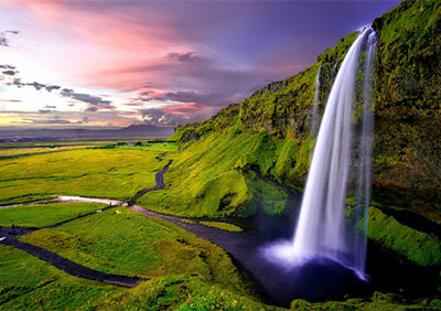 A stunning waterfall coming down from a green covered mountain